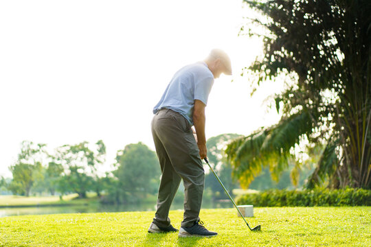 Elderly Asian man enjoying the morning round of golf in soft and warm sunlight. - Powered by Adobe