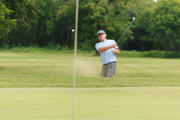Elderly Asian man enjoying the morning round of golf in soft and warm sunlight.