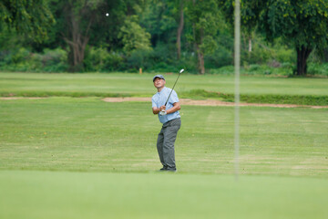 Obraz premium Elderly Asian man enjoying the morning round of golf in soft and warm sunlight.