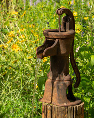 A old hand operated water pump in a meadow with flowers in the background