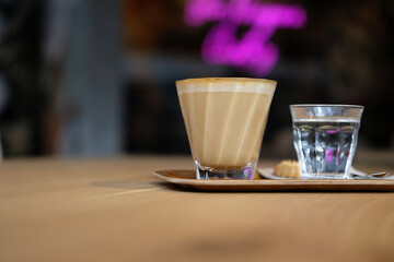 Flat white with water and cookie on wooden tray in modern café – cozy coffee break, relaxing...