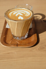 Flat white close-up served on a wooden tray, accompanied by a glass of water and a small cookie, placed on a table in a modern café.