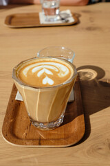Flat white served on a wooden tray, accompanied by a glass of water and a small cookie, placed on a table in a modern Andorra café.