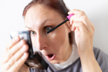 Woman applying mascara with surprised expression looking in mirror