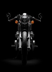 Shiny black motorcycle stands in the dark. Chrome parts reflect the light strongly.
