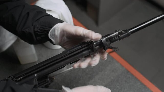 Close up shot of gloved hands of anonymous expert disassembling parts of rifle in shooting club