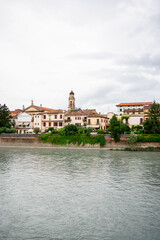 A scenic view of Verona along the Adige River, with historic buildings and lush hills in the background on a cloudy day