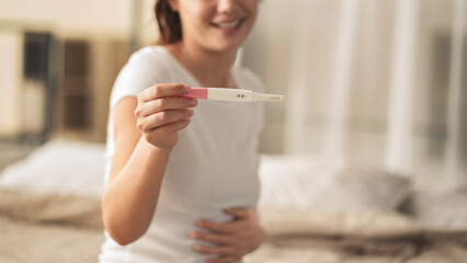 A woman holding a pregnancy test. She is smiling and she is happy about the result