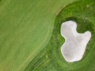 Scenic aerial view of a coastal golf course with green fairways, sand bunkers, golf carts, and players, surrounded by lush vegetation and turquoise sea