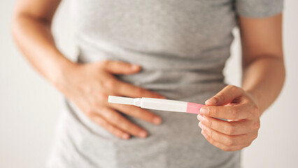 A woman holding a pregnancy test. She is smiling and she is happy about the result