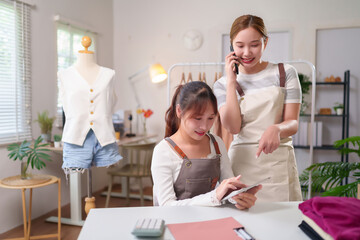 Asian Women Discussing Fashion Design Business on Tablet and Phone in Studio or Workshop For Online Sale Clothing