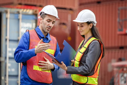 Engineer and foreman worker team in hardhat and safety vest working at containers cargo, Engineers team with clipboard managing cargo operations, Teamwork concepts