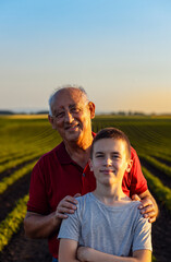 Portrait of senior farmer with his grandson standing in green soybean field and looking at camera.