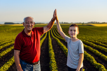 Portrait of senior farmer with his grandson standing in green soybean field and looking at camera.