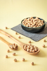 Healthy dried chickpeas in wooden spoons and ceramic bowl on pastel background. Rustic food arrangement with natural light