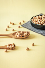 Minimalist composition with chickpeas in wooden spoons and ceramic bowl on warm pastel background. Healthy and natural food concept