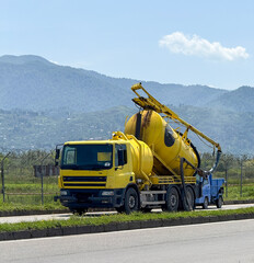 Yellow Cement Mixer Truck with Attached Boom Arm on Rural Road © Aleksandr