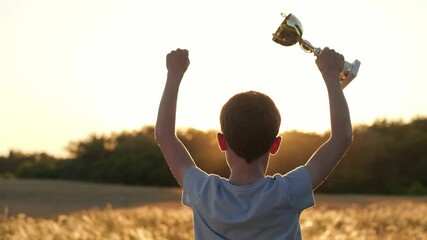 Child raises trophy cup at sunset, family celebrating success. Child stands proud with trophy raised high, symbolizing child achievement, proud family moment. Child represents growth, support family.