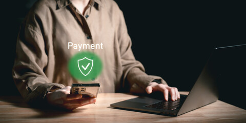 Close-up of a person holding smartphone near laptop with secure payment icon glowing, illustrating safe online payment approval