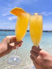 woman holding a cocktail mimosas and beach in background
