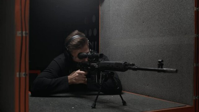 Stab shot of Caucasian man wearing goggles and earmuffs shooting rifle at indoor range