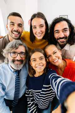 Vertical photo of large group of cheerful family members taking a selfie together, smiling and looking at camera enjoying time at home.