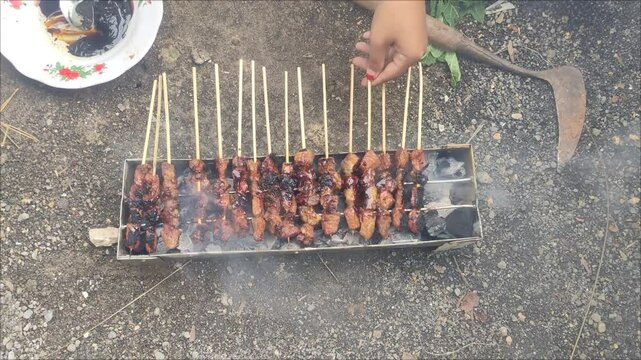 Someone is cooking satay meat. Meat on the grill. Meat is grilled on skewers. Cooking satay