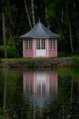 Fototapeta premium Cozy cabin nestled in a forest by a calm lake, perfectly reflected in the still water. A peaceful retreat surrounded by nature, capturing serenity, solitude, and natural beauty.
