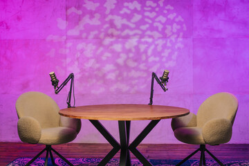 Podcast recording setup with modern chairs and microphones illuminated by colorful lights