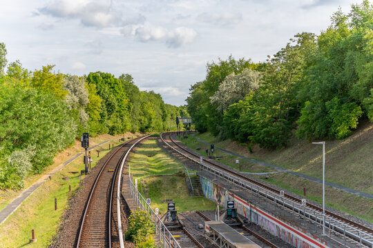 A double-track railway line runs through a green forest. The tracks curve gently into the distance.