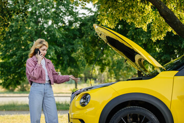 A young woman calls her husband on the phone for help near a broken down new car. Concerned woman...