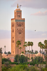 Obraz premium Koutoubia Mosque with its iconic minaret at dusk in Marrakech. Ancient architecture surrounded by palm trees. Scenic view of cultural landmarks and historical sites.