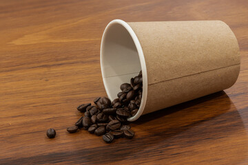 Disposable coffee glass or cup with natural coffee beans on wooden background 