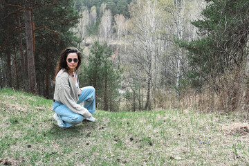 Girl with glasses grey knitted jacket on a forest background.