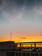 A vibrant sunset bathes the sky in hues of orange and pink, casting a warm glow over silhouetted buildings, creating a serene and picturesque urban skyline.
