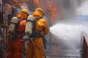 Two firefighters in protective gear combat a fire on a ship, utilizing air tanks as they actively extinguish the flames