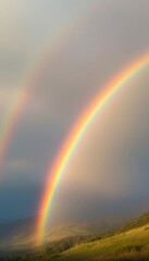 Fototapeta premium Vibrant Rainbow Arches Over Grassy Hills After Rainstorm Showing Double Rainbow Effect
