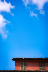 Traditional tiled roof and shuttered windows of red house under vibrant blue sky with copy space