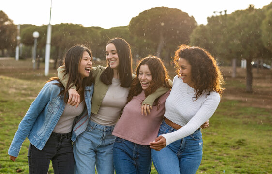 Four young women laughing and hugging in a park