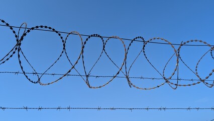Weathered barbed wire coils creating geometric shapes, casting sharp shadows against bright azure...