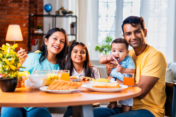 Indian family having breakfast on dining table with baby and daughter in bright modern home