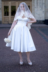 Bride have her face covered by a veil. Full length portrait of beautiful young bride in white short...