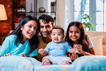 Smiling Indian family sitting on floor near sofa, bonding together in stylish cozy living room