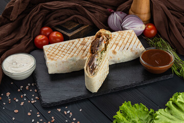 Shawarma, Kebab, Doner in lavash with fresh vegetables on a black tray with two sauces