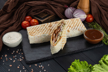 Shawarma, Kebab, Doner in lavash with fresh vegetables on a black tray with two sauces