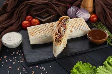 Shawarma, Kebab, Doner in lavash with fresh vegetables on a black tray with two sauces