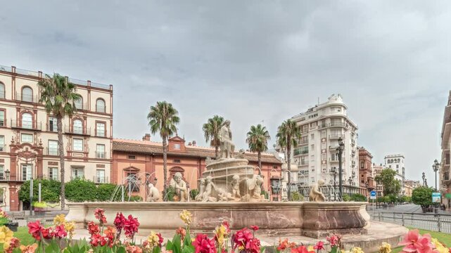 Hispalis Fountain in Seville, one of the city's most beautiful fountains, surrounded by colorful flowers and historical buildings. Timelapse hyperlapse with a cloudy sky in the background.