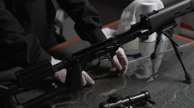 Close up shot of gloved hands of unrecognizable specialist disassembling rifle at table indoors