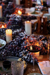 Elegant table display for a wine and cheese gathering. A glass of red wine, assorted cheeses, and clusters of grapes adorn the table, accentuated by glowing candlelight.