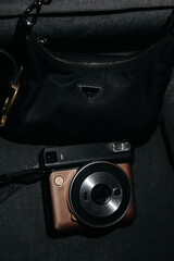 Close-up of a vintage-style instant camera and a luxury designer bag placed together in dim...